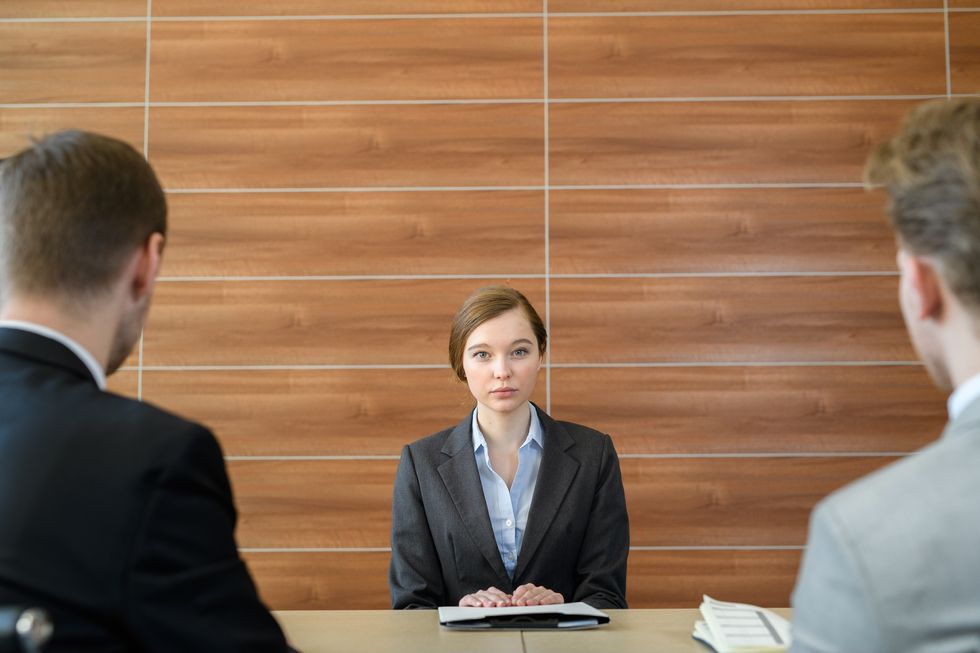 portrait of serious worried young female job candidate sitting at table with employers and listening to their questions at job interview