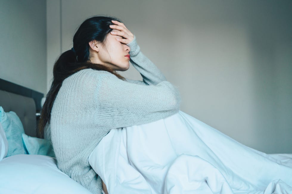 portrait of sickness woman sitting alone on the bed in the bedroom, self isolation herself during coronavirus pandemic outbreak