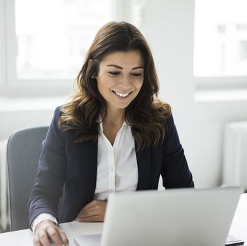 portrait of smiling businesswoman sitting at desk in the office working on laptop