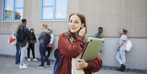 Portrait of smiling female student carrying laptop while standing at university campus with friends in background