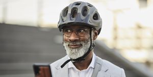 portrait of smiling mature businessman with smartphone wearing cycling helmet and glasses