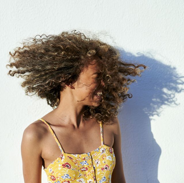 portrait of smiling woman with curly hair, in front of white wall