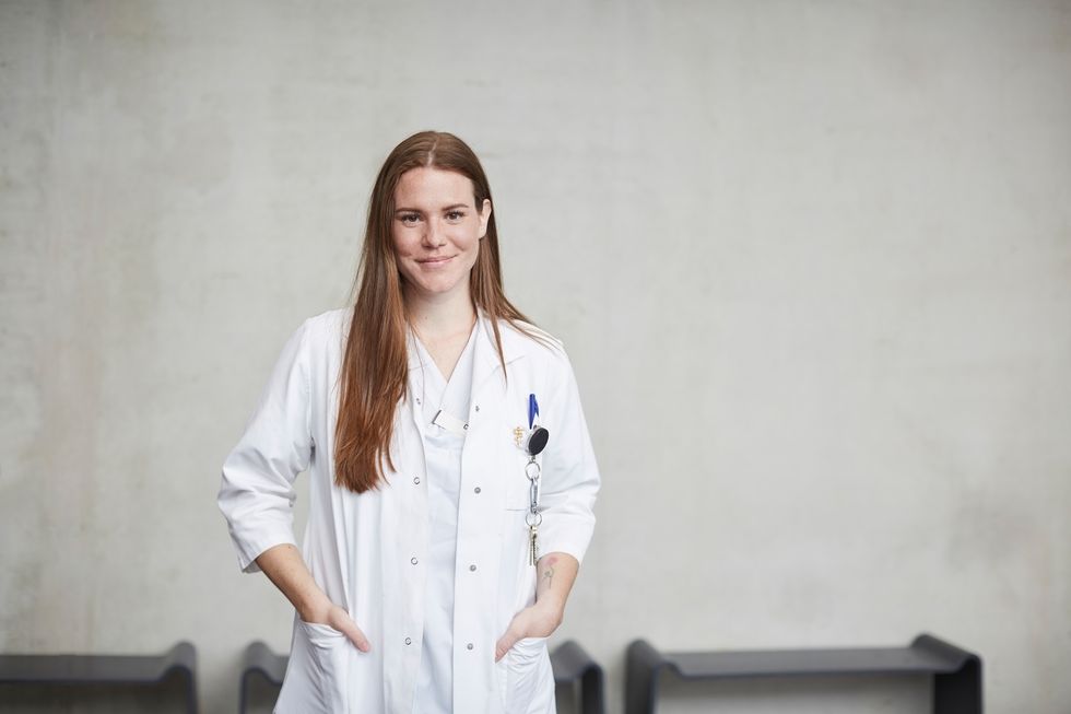 portrait of smiling young female brunette doctor standing with hands in pockets at hospital