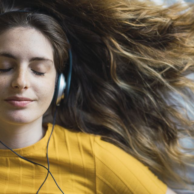 portrait of smiling young woman lying on bed listening music with headphones