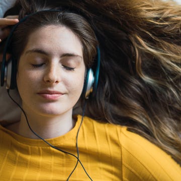 portrait of smiling young woman lying on bed listening music with headphones