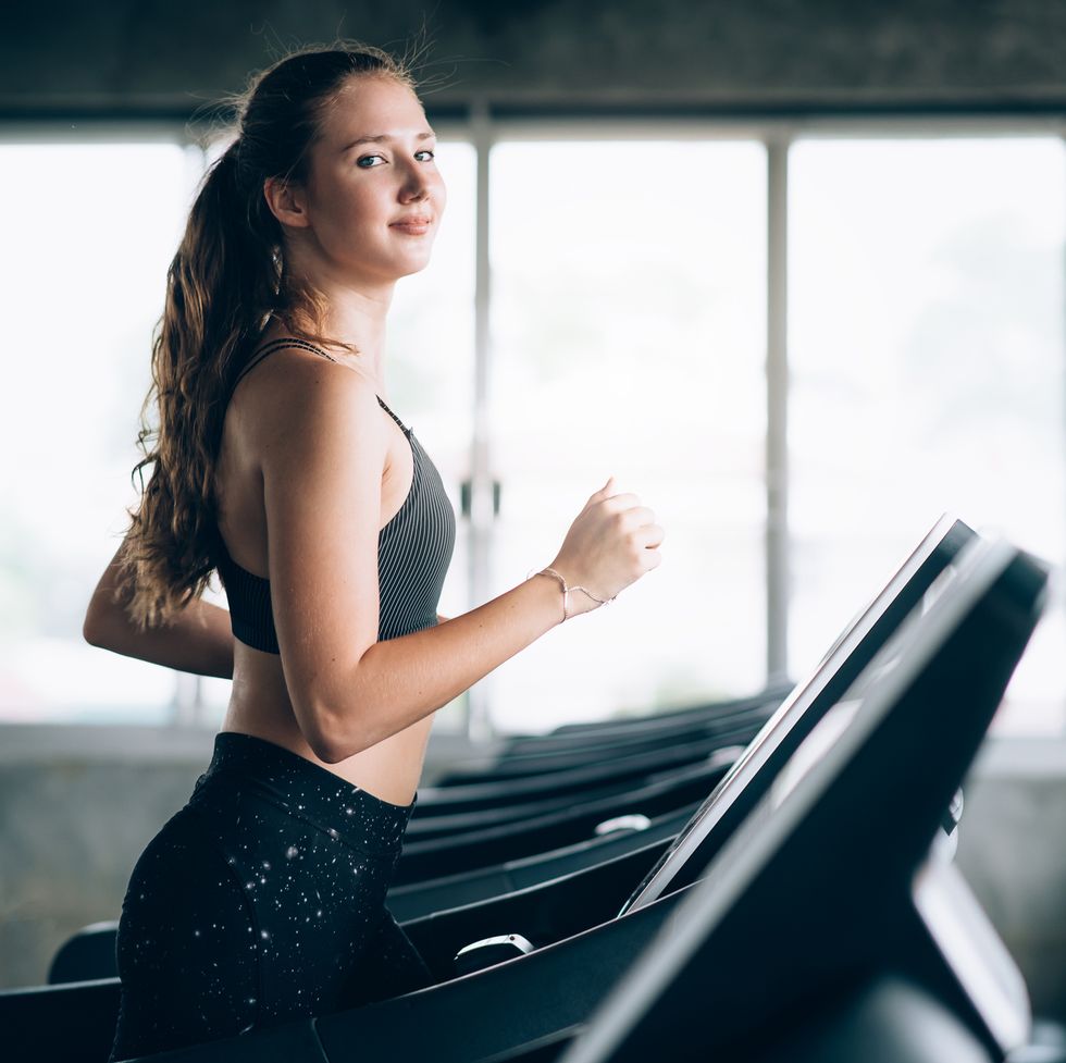 Portrait Of Smiling Young Woman Running On Treadmill