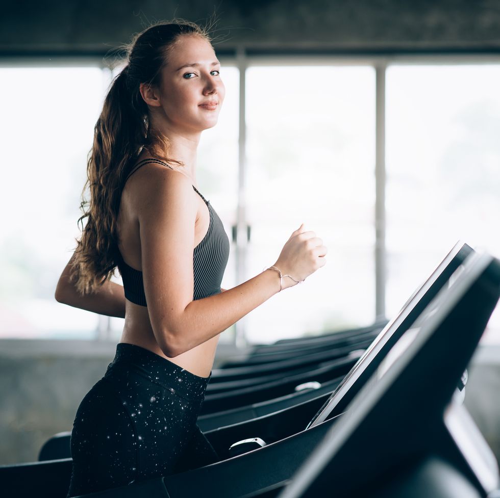 Portrait Of Smiling Young Woman Running On Treadmill