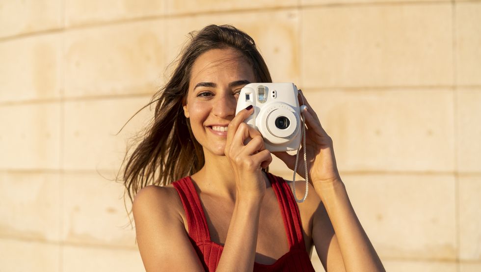 Portrait of smiling young woman taking instant photo outdoors