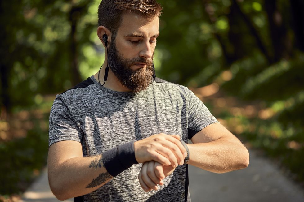 portrait of sporty man with earphones in forest checking his smartwatch