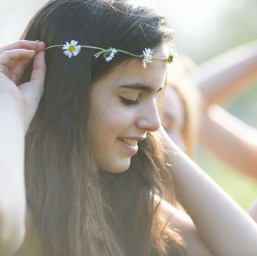 portrait of teenage girl putting on daisy chain headdress in park