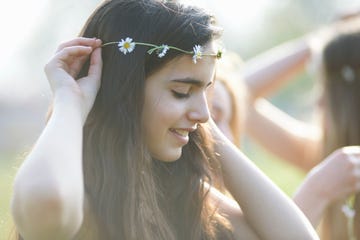 portrait of teenage girl putting on daisy chain headdress in park