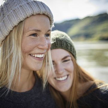 Portrait of two smiling female friends wearing knit hats at the riverbank