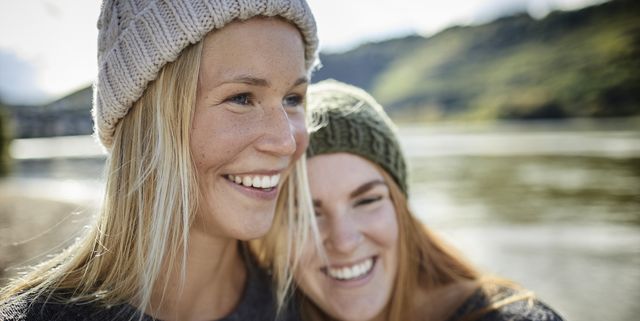 Portrait of two smiling female friends wearing knit hats at the riverbank