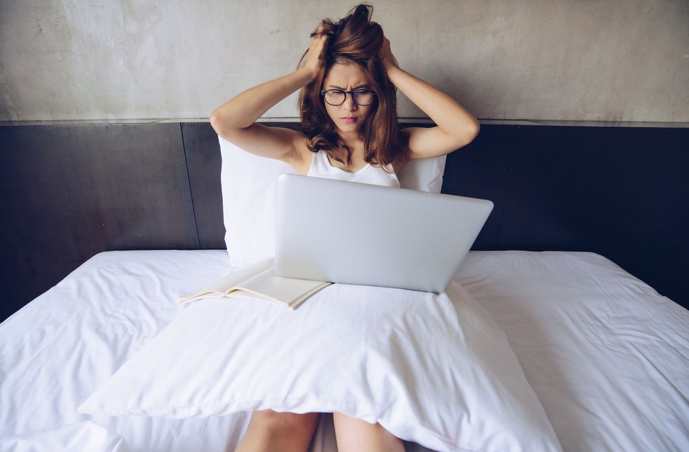 portrait of woman sitting on bed and working on her laptop, look like she worry about her jobs