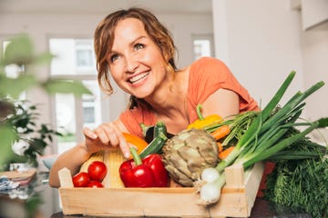 una mujer posa con una caja de hortalizas y verduras