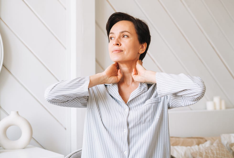 portrait of young adult brunette woman doing facial massage with hands in bedroom at home, morning skincare routine