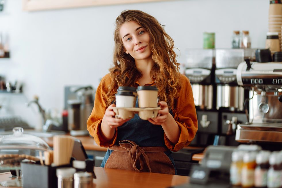 portrait of young barista woman serving coffee with a big smile