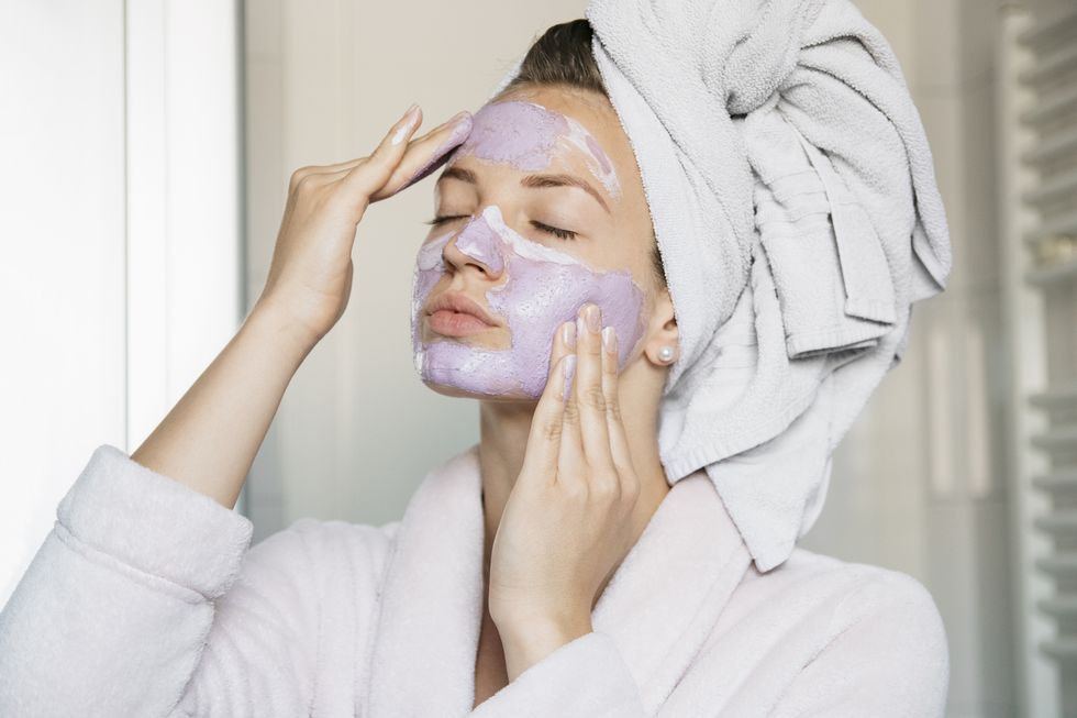 portrait of young beautiful woman with a facial mask having a spa treatment at home