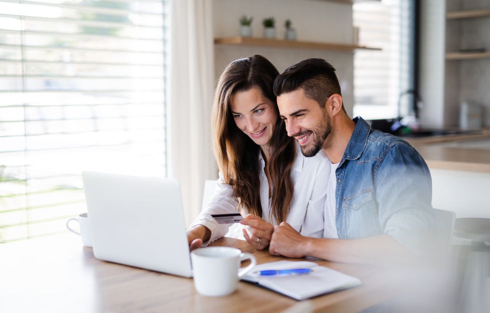 portrait of young cheerful couple with laptop indoors at home, making online payment