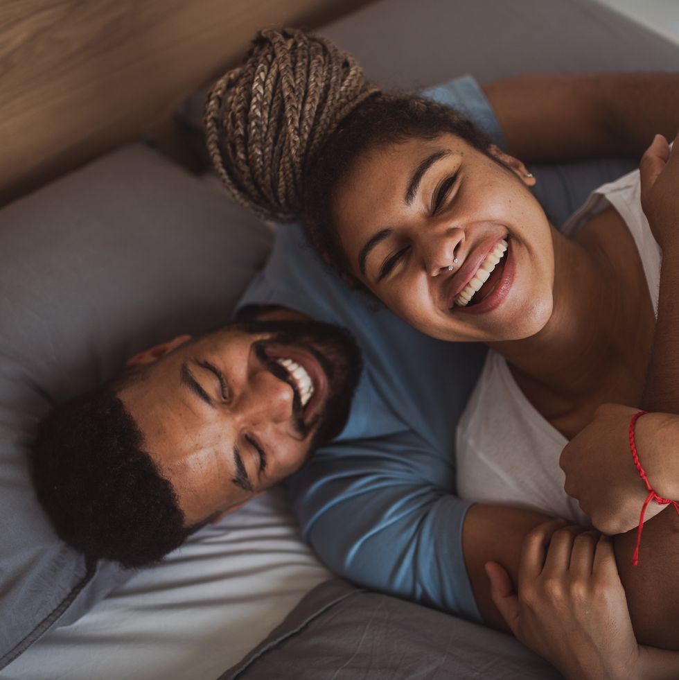 portrait of young couple playing on bed indoors at home, laughing