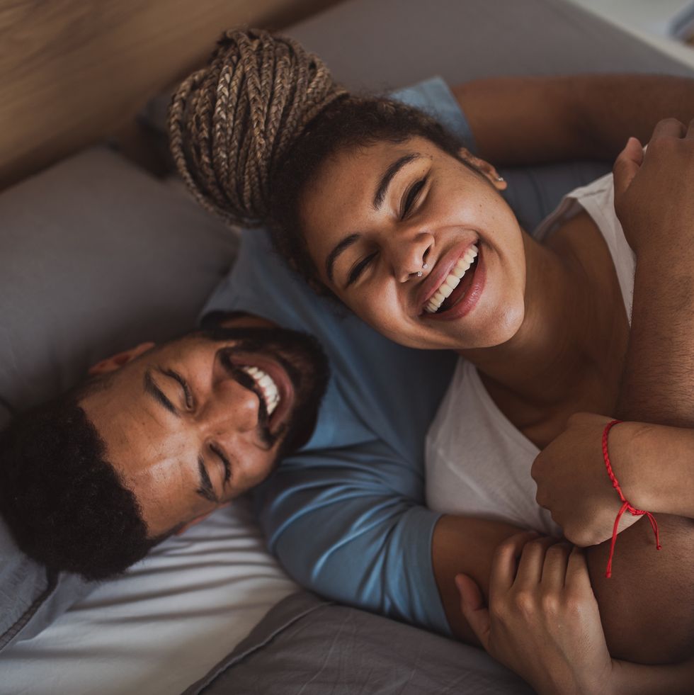 portrait of young couple playing on bed indoors at home, laughing at funny good morning message