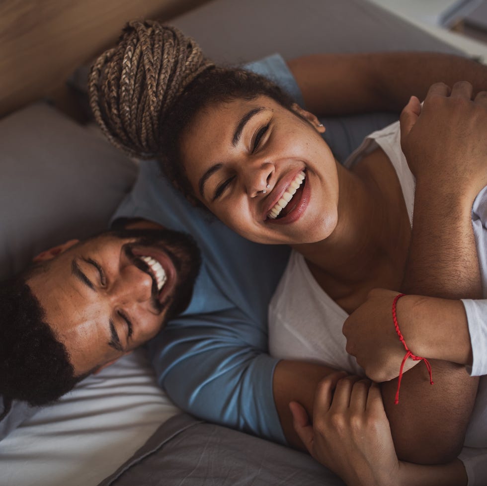 portrait of young couple playing on bed indoors at home, laughing