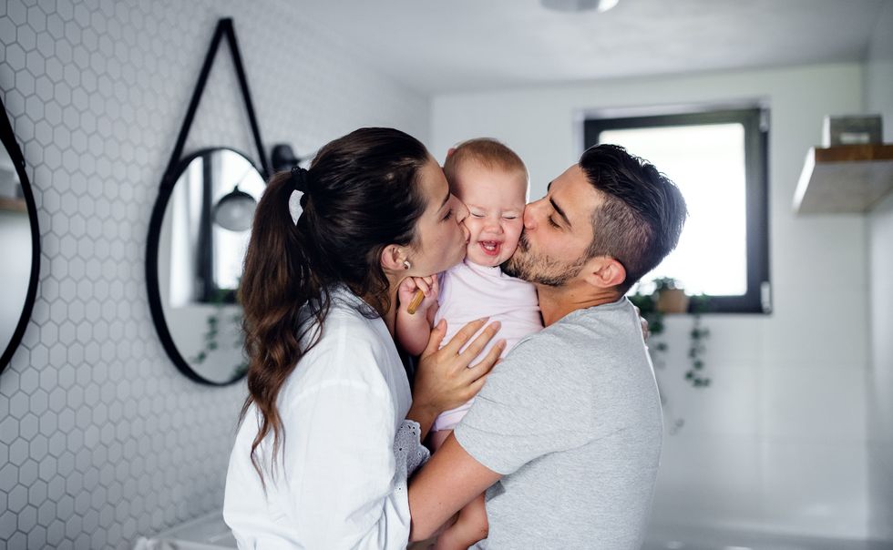portrait of young couple with toddler girl in the morning indoors in bathroom at home, kissing