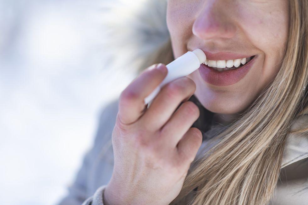 Portrait of young female applying lip balm in winter.