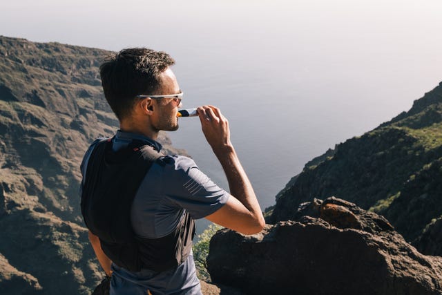 portrait of young man drinking energy sports nutrition energy gel while sitting and resting after trail running