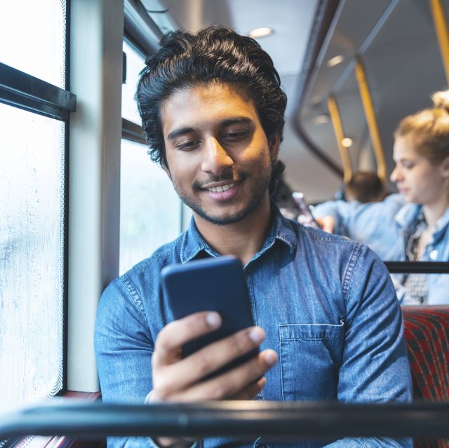 portrait of young man travelling by bus looking at cell phone, london, uk
