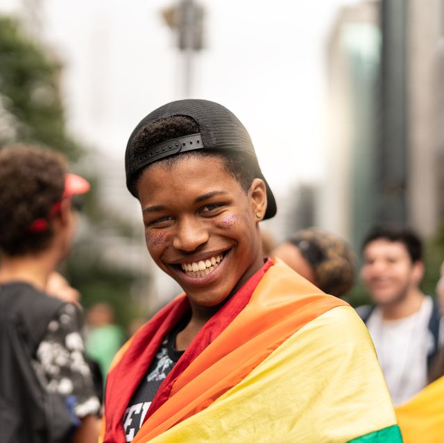 Portrait of young man with rainbow flag with friends on background at Gay Parade