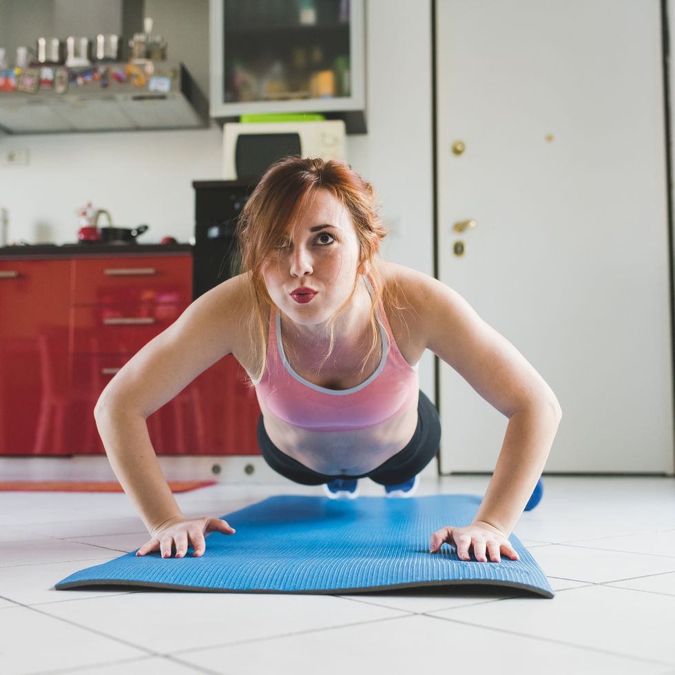portrait of young woman doing push ups on kitchen floor