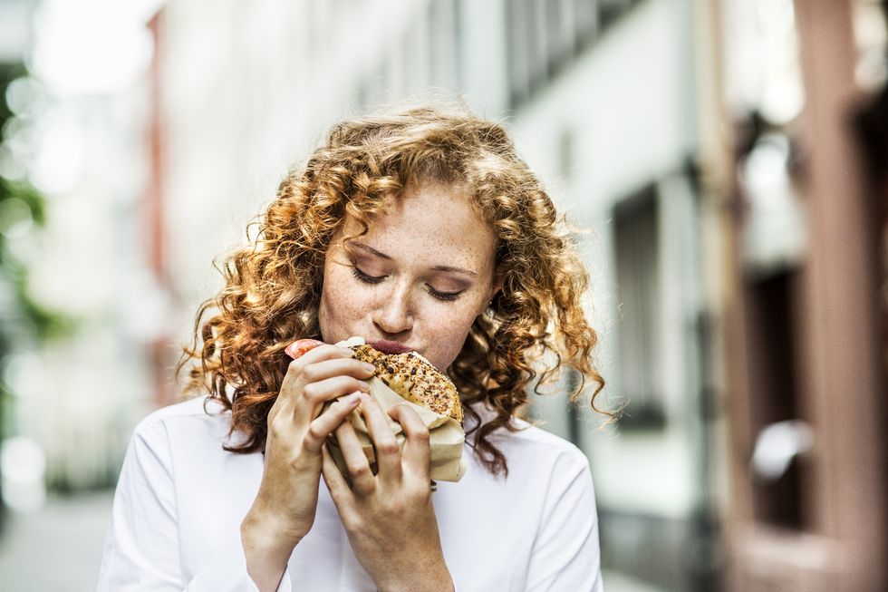 portrait of young woman eating bagel outdoors