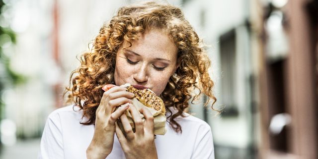 Portrait of young woman eating bagel outdoors