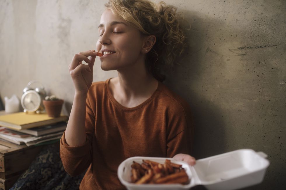 portrait of young woman eating french fries at home