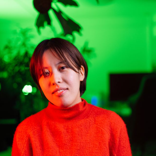 portrait of young woman her face lit by red neon light in green lit room at home