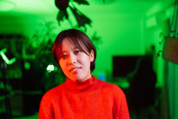 portrait of young woman her face lit by red neon light in green lit room at home