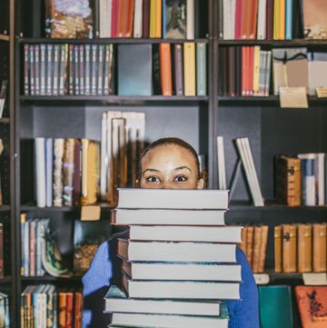 portrait of young woman holding stack of books while standing in bookstore