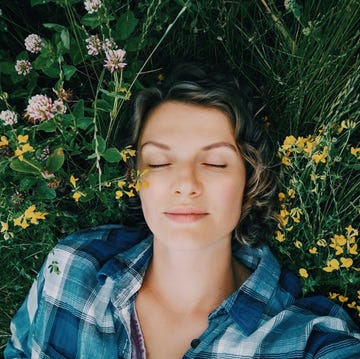 Una mujer tumbada entre plantas en un campo una mujer posa con una camisa de cuadros tumbada sobre unas plantas y flores