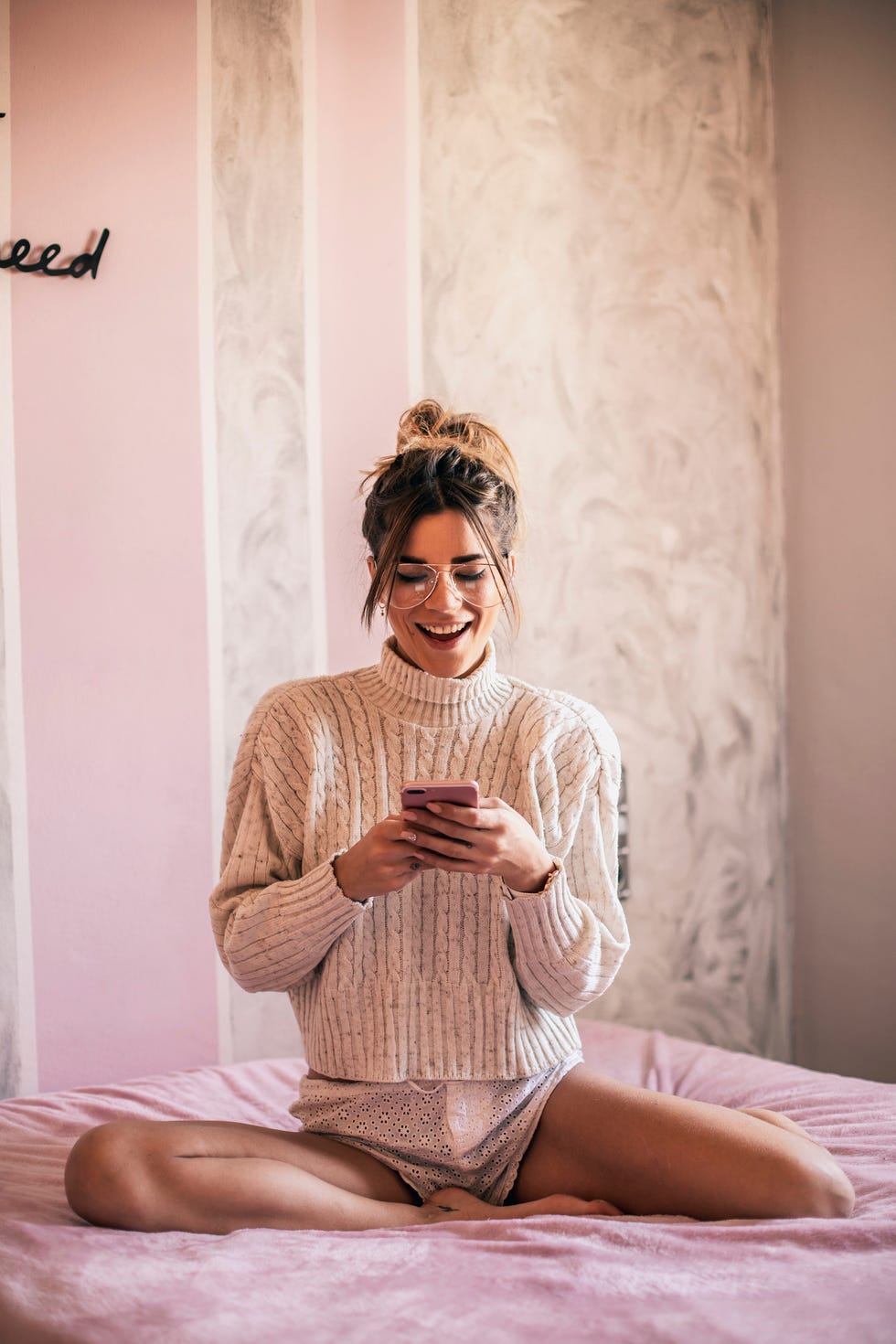 portrait of young woman sitting on bed text messaging