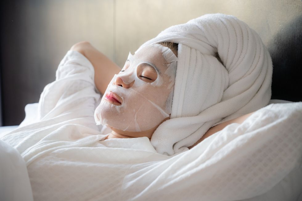 portrait of young woman sleeping on bed while applying facial mask on her face
