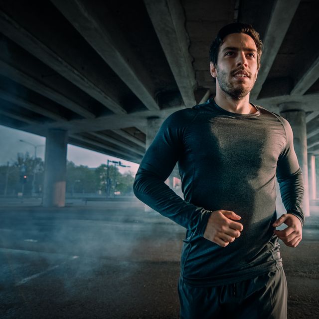 Portrait Shot of an Athletic Muscular Young Man in Sports Outfit Jogging in the Street. He is Running in an Urban Environment Under a Bridge.