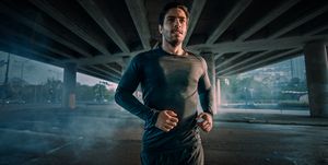 Portrait Shot of an Athletic Muscular Young Man in Sports Outfit Jogging in the Street. He is Running in an Urban Environment Under a Bridge.