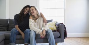Portrait smiling barefoot lesbian couple hugging on sofa