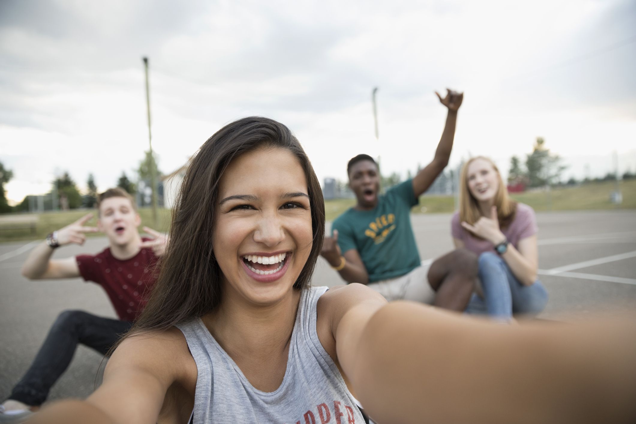 Portrait smiling teenage girl with friends taking selfie on outdoor basketball court