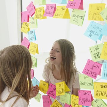 caucasian girl laughing in mirror with positive affirmation adhesive notes around the mirror