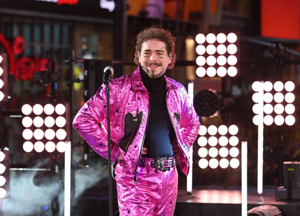 post malone smiles while standing on a stage behind a microphone on a stand