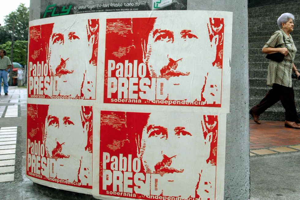a city street with a poster showing a presidential election advertisement and four photos of pablo escobar