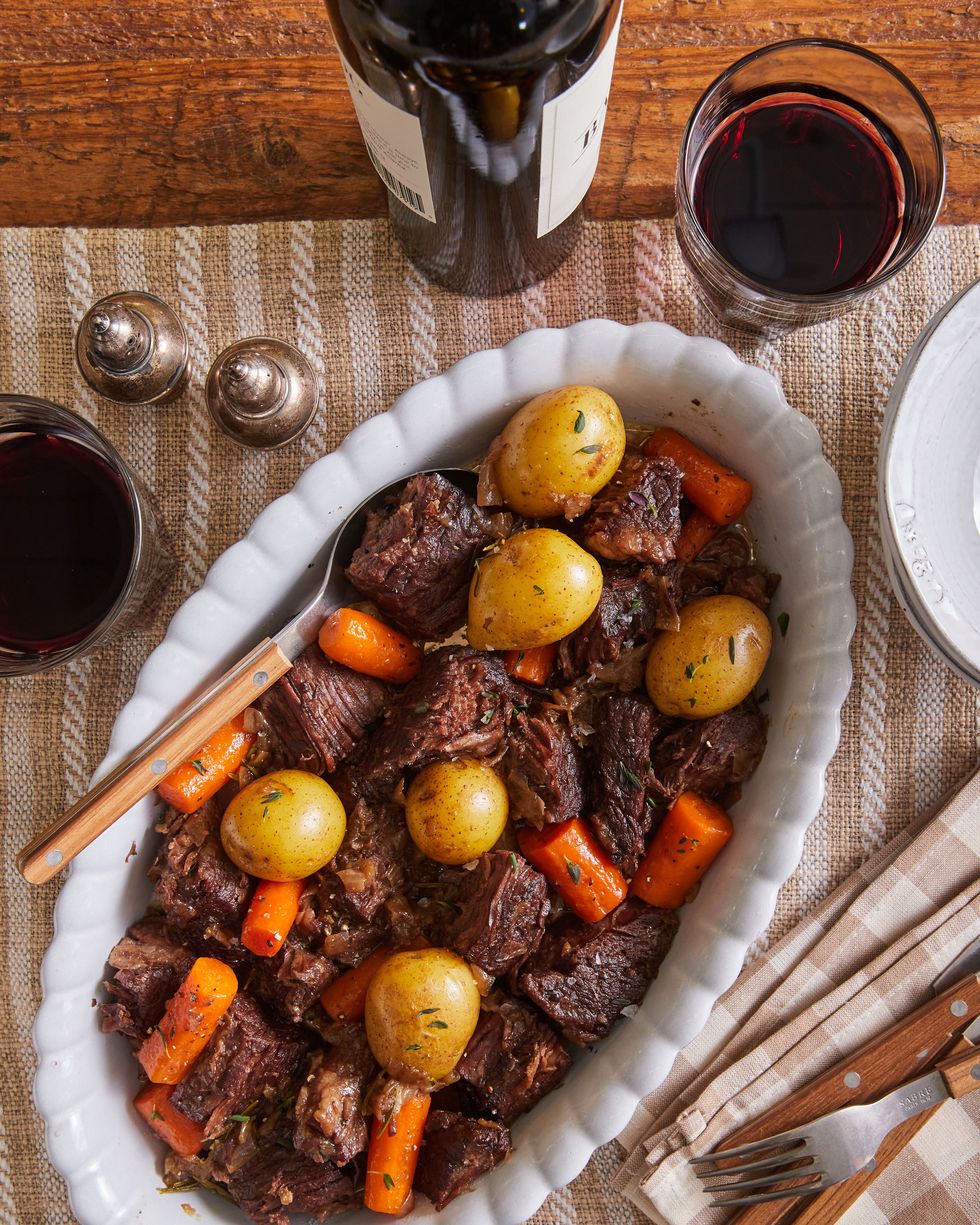 pot roast with carrots and onion on a platter with glasses of wine nearby