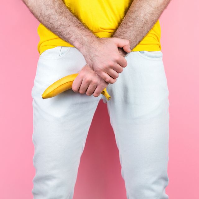 potency and men's health a man in white jeans, legs apart, holds a banana near the genitals pink background close up of hands
